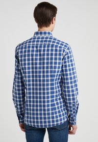 Camicia a maniche lunghe con un motivo a quadri blu e bianchi, colletto button-down e orlo leggermente curvato con polsini abbottonati.