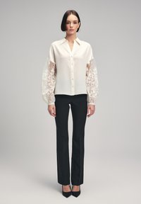 White blouse with sheer lace puff sleeves, button front, and collar, paired with black tailored pants and pointed toe heels.