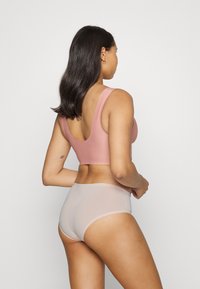 Rosa sömlös sportbehå med breda axelband, i kombination med ljusrosa hipster underkläder. Slät tyg och åtsittande design.