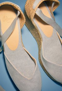 Espadrilles compensées en tissu bleu clair avec semelles intérieures beige rembourrées et semelles en jute tissée sur une surface bleu clair.