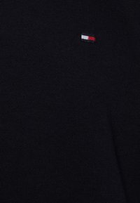 Un pull en maille bleu marine avec un petit logo brodé tricolore (rouge, blanc, bleu) situé dans le coin supérieur gauche.