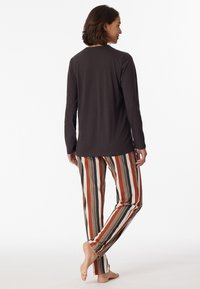 Langärmliges dunkles Oberteil, kombiniert mit gestreiften Hosen in Orange, Schwarz, Creme und Grau. Weicher Stoff, lockere Passform, sichtbare Nähten.