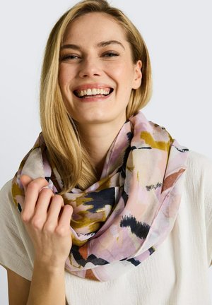 Femme souriante aux cheveux blonds portant un haut blanc et une écharpe multicolore à motif abstrait, tenant un coin de l’écharpe près de son épaule.