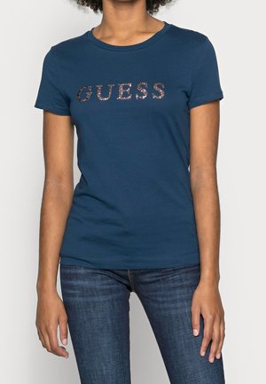 Marineblå kortærmet t-shirt lavet af blød bomuld med en glitrende "GUESS"-logo på brystet. Tætsiddende design med rund hals.