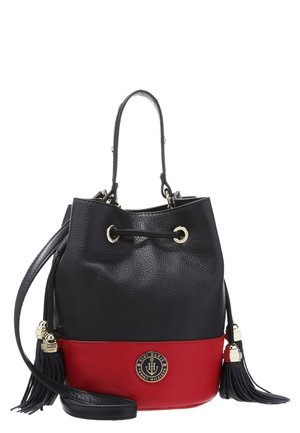 Petit sac seau en cuir noir et rouge avec fermeture par cordon, longue bandoulière, pompons et badge rond avec logo Tommy Hilfiger sur le devant.
