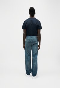 Μπλε κοντομάνικη μπλούζα σε σκούρο ναυτικό χρώμα, συνδυασμένη με άνετο τζιν παντελόνι σε ανοιχτή μπλε απόχρωση, με πέντε τσέπες και ορατές λεπτομέρειες ραφής. Λευκά αθλητικά παπούτσια.