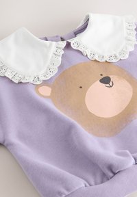 Felpa viola con stampa di una faccia da orso; presenta un collo con colletto in pizzo bianco e una texture morbida, adatta per un abbigliamento casual.