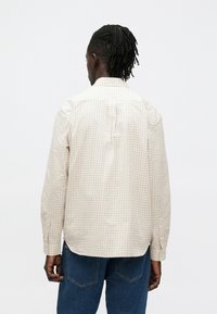 Svetlo bež karo srajca z dolgimi rokavi, gumbi na manšetah in oprijetim hrbtom. Iz bombaža, s klasičnim ovratnikom in ravnim spodnjim robom.