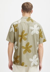 Camisa de manga corta de color verde claro con grandes patrones abstractos de flores en blanco y marrón. Hecha de una suave tela texturizada.