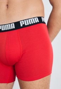 Boxeri roșii cu o textură netedă și un brâu elastic negru, având logo-ul "PUMA" în alb, punând în evidență designul și potrivirea.