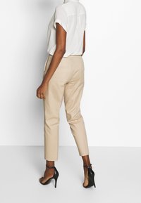 Beżowe, dopasowane spodnie z przednimi kieszeniami, zestawione z lekką, krótkim rękawem bluzką. Całość dopełniają czarne sandały na wysokim obcasie.