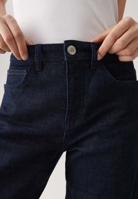 Donkerblauwe denim jeans met knoopsluiting, vijf-pocket ontwerp en contrasterende stiksels. De stof heeft een zachte textuur en een lichte rek.