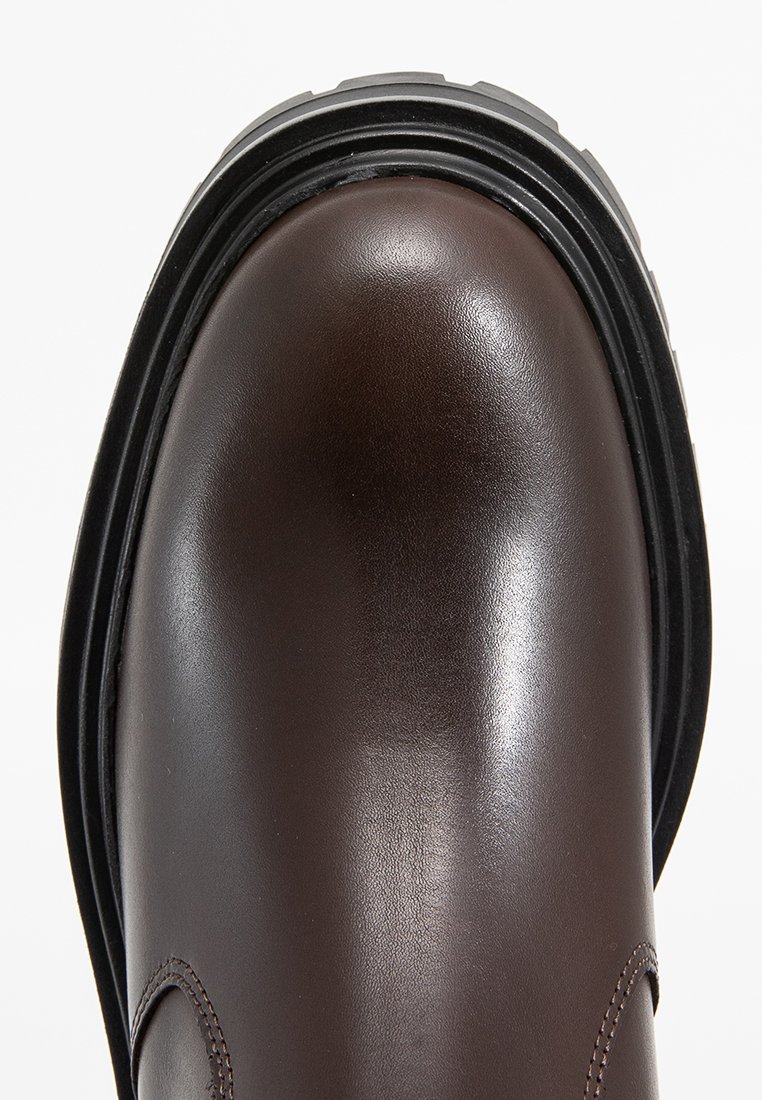 Braune Lederstiefel mit einer glatten Oberfläche, runder Zehenpartie und einer dicken schwarzen Gummisohle. Verfügt über dezente Nähte entlang der Kanten.