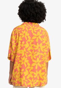 Short-sleeved shirt in pink fabric adorned with large yellow floral pattern. Relaxed fit with a collar and visible stitching details.