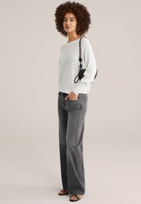 Pull gris clair côtelé avec des rayures horizontales ; associé à un jean gris foncé à jambes larges. Sac à épaule noir et sandales à brides complètent le look.