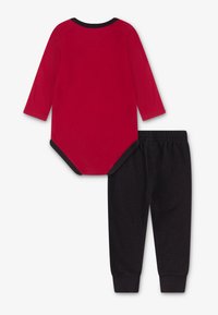 Body rouge à manches longues avec des bordures noires, associé à un pantalon noir à motif moucheté, fabriqué dans un tissu doux et confortable.