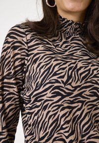 Långärmad topp i beige tyg med svart zebramönster, strukturerad ribbad design och en hög, smockad halsringning.