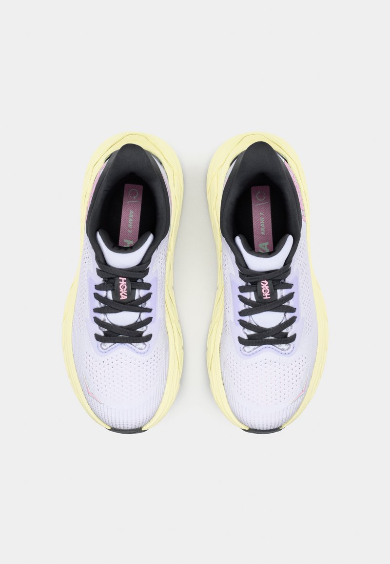 Zapatillas de running para mujer con un upper de malla de color púrpura claro, cordones negros y una entresuela amarilla. Cuentan con un cuello acolchado y plantillas con marca.