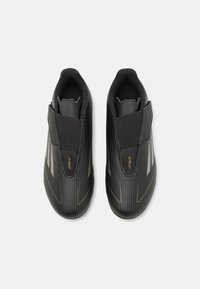 Melni sporta apavi ar elegantu dizainu, ar teksturētu augšējo daļu, velcro siksniņu un zelta akcentiem, ar ribotu detaļu gar sāniem.