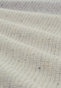 Texturiertes Gewebe in Creme mit subtilen Sprenkeln in Orange und Lila, das ein geripptes Muster und ein weiches, gestricktes Aussehen aufweist.