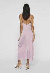Lång, ärmlös klänning i rosa satin med V-formad ryggdesign, slät textur och ankel-lång skärning. Matchad med sandfärgade klackar med remmar.