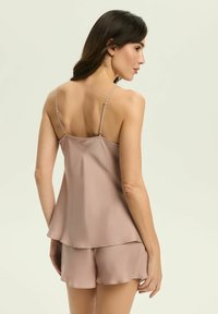 Jasnoróżowa satynowa koszulka na ramiączkach z regulowanymi paskami oraz dopasowane szorty z falbaniastym wykończeniem, gładką fakturą i luźnym krojem.
