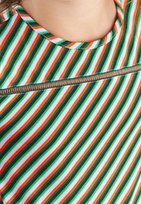 Striped t-shirt featuring green, orange, and white vertical lines. Round neckline with exposed stitching and a horizontal zipper detail across the chest.