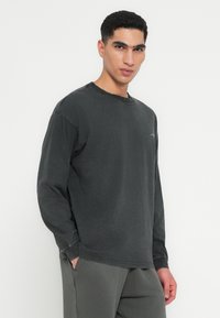 Czarny szary longsleeve w luźnym kroju, z okrągłym dekoltem i detalami szwów. Materiał ma postarzany teksturę.