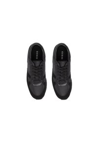 Un par de zapatillas negras de la marca Guess con cordones, vistas desde arriba sobre un fondo blanco.