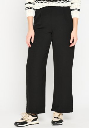 Zwarte wijde broek van zachte stof, met een gladde textuur en twee zijzakken. Gemaakt met beige en zwarte sport sneakers.