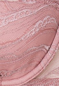Čipkasti bralette u prašnjavo ružičastoj boji s složenim valovitim uzorcima, sjajnim naglascima i teksturiranom površinom, s mekanim rubovima i delikatnim šavovima.