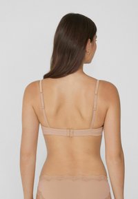 Světlý béžový podprsenka s nastavitelnými ramínky, zapínáním na háček a očko a hladkým materiálem. Čipkový lem na pasu. Jednoduchý, minimalistický design.