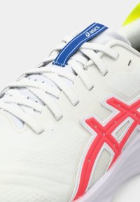 Nærbilde av hvite Asics løpesko med hvite snørebånd, blå merke pynt på tungen, og rød logostripe på siden.