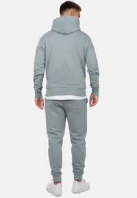 Lichtgrijze hoodie en bijpassende joggers, gemaakt van zachte stof. Bevat een capuchon, ribgebreide manchetten en zijzakken. Strakke witte sneakers maken de look compleet.