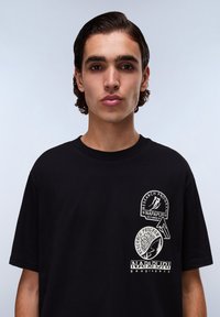 Černé bavlněné tričko s bílými grafikami, včetně log a designů, na levé části hrudi a na rukávu, s kulatým výstřihem.