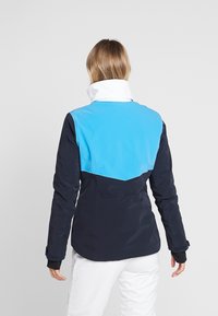 Tmavě modrá bunda se světle modrou horní částí, bílým límcem a černými akcenty. Vyrobená z hladké, voděodolné látky, s přiléhavým střihem.