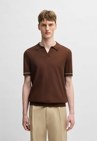 Brun kortärmad polo med V-formad krage, prydd med kontrasterande vita kanter på ärmarna. Mjuk, strukturerad stickad tyg.