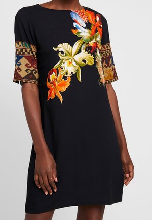 Zwarte jurk met kleurrijke grote bloemenprint aan de voorkant, met geometrische patronen op de korte mouwen, gedragen door een persoon met een donkere huidtoon.