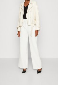 Blouson en cuir blanc avec quincaillerie argentée, associé à un pantalon blanc loose et des escarpins noirs à bout pointu. Top noir à col en V sous le blouson.