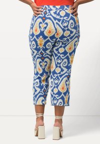 Pantalons Capri à motifs bleus avec des designs blancs, jaunes et oranges. Ils offrent une texture lisse et une taille agrémentée de boutons orange.