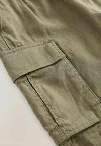 Zielona lniana tkanina o teksturowanym wykończeniu z kieszenią na rękawie. Szczegółowe st stitching wzdłuż szwów podnosi trwałość.