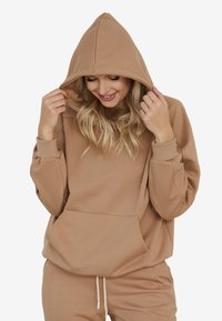 Przesadzony beżowy hoodie z kapturem na sznurku, prążkowanymi mankietami i przednią kieszenią typu kangaroo. Miękka faktura materiału i luźny krój.