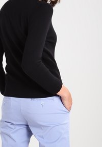 Svart stickad tröja med långa ärmar, kombinerad med ljusblå byxor med bakfickor och knappdetaljer.