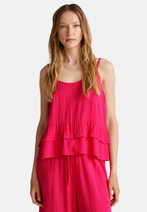Top de tirantes en fucsia, con capas y tirantes ajustables, que presenta una tela texturizada y un diseño fluido, combinado con pantalones de corte holgado.