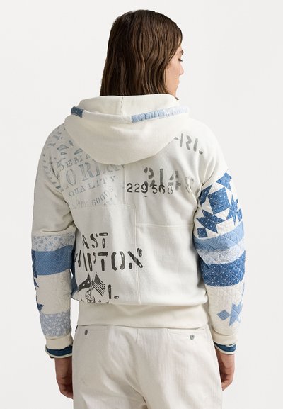 Pelēka kapuce ar off-white krāsu un ziliem kviltotiem piedurknēm, kas izceļ ģeometriskus rakstus un drukātas grafikas. Mīksts audums ar teksturētām akcentiem.
