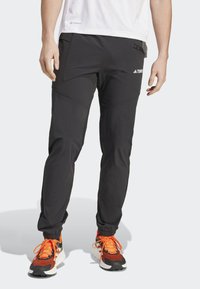 Czarne sportowe spodnie o tapered design, z zamykanymi na zamek kieszeniami i elastycznymi mankietami. Wykonane z lekkiego materiału, idealne do aktywności fizycznej.