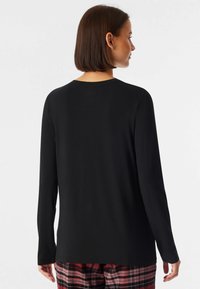 Maglietta nera a maniche lunghe con scollatura rotonda, realizzata in tessuto morbido. Caratterizzata da una vestibilità comoda, abbinata a pantaloni del pigiama a quadri rossi.