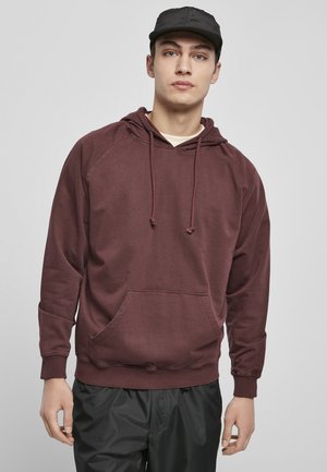 Marron hættebluse med frontlomme, ribbede manchetter og kant, der har snortræk. Bæres med sorte tapered bukser.