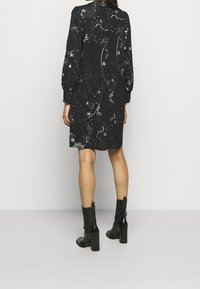 Černé šaty s dlouhými buclatými rukávy, ozdobené nebeským vzorem. Nosené s černými kotníkovými botami, zobrazené zezadu na bílém pozadí.