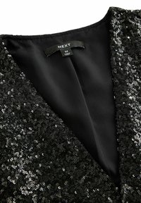 Robe noire à sequins, avec un décolleté en V profond, intérieur doublé et texture lisse. Étiquette visible, indiquant la taille M par NEXT.